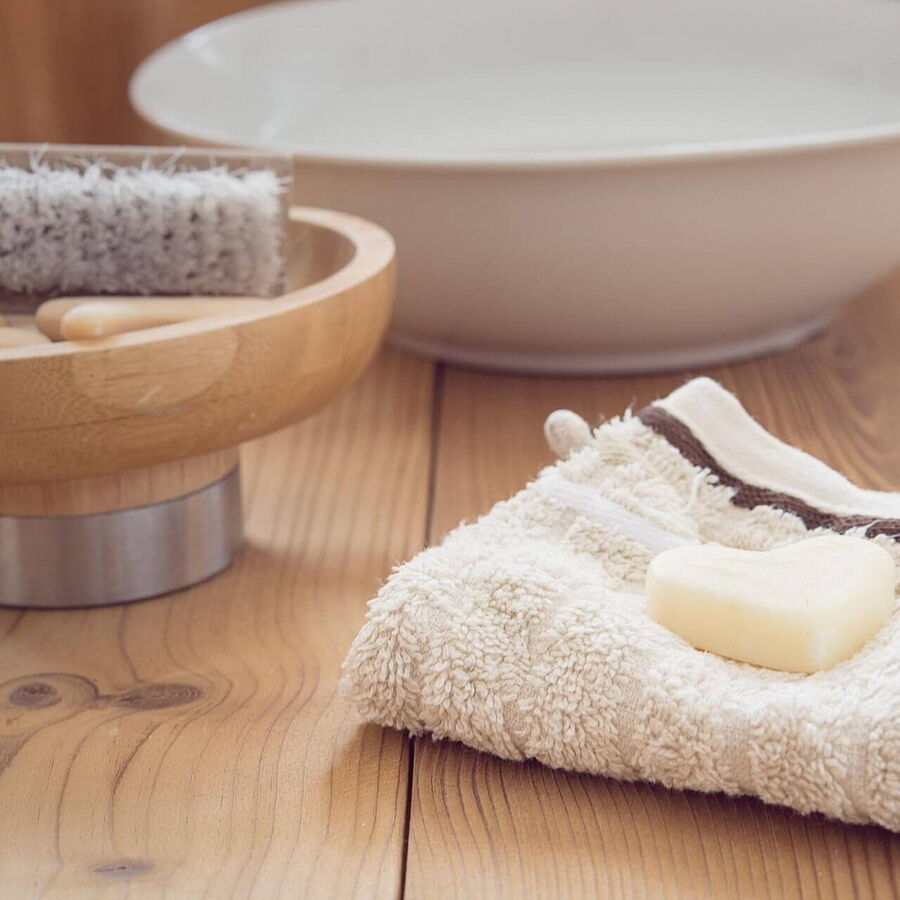 Im Badezimmer auf der Holzablage ist eine Schüssel mit Nagelbürste, ein Waschlappen mit Herzseife darauf liegend und einer Keramikschüssel mit Wasser schön angerichtet..
