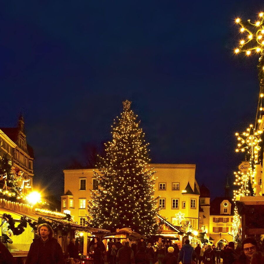 Christkindlmarkt in der Adventszeit: Verkaufsstände mit weihnachtlichen Dekorationen, Kunsthandwerk und regionalen Spezialitäten, umgeben von festlicher Beleuchtung und einer historischen Kulisse.